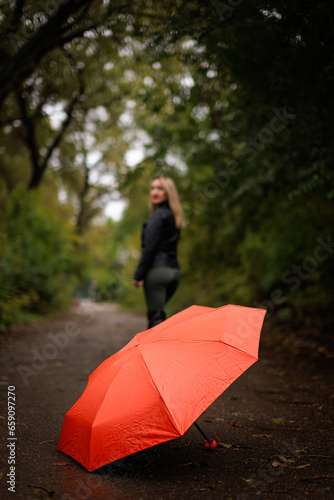 Fototapeta Naklejka Na Ścianę i Meble -  In the foreground is a red umbrella against a girl in the distance.  A red umbrella in the fall