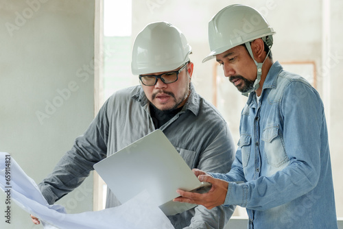 Bearded Indian engineer wearing helmet Stand and give orders to the foreman. Follow plan in blueprint. Let workers rush to build houses in the construction area. Cooperation of people of multiracial