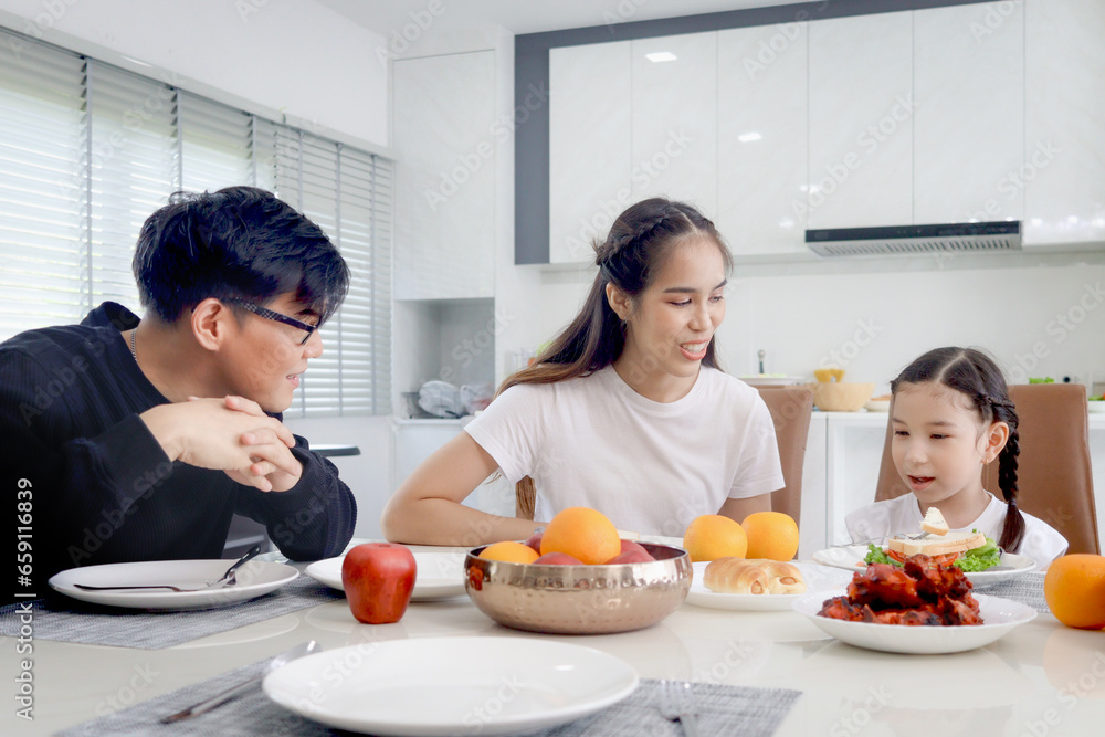 Happy family has meal in dining room. Parents, mother father and kid daughter sit at dining table and have fun during breakfast or lunch. Cheerful family enjoy eating food and spending time together.