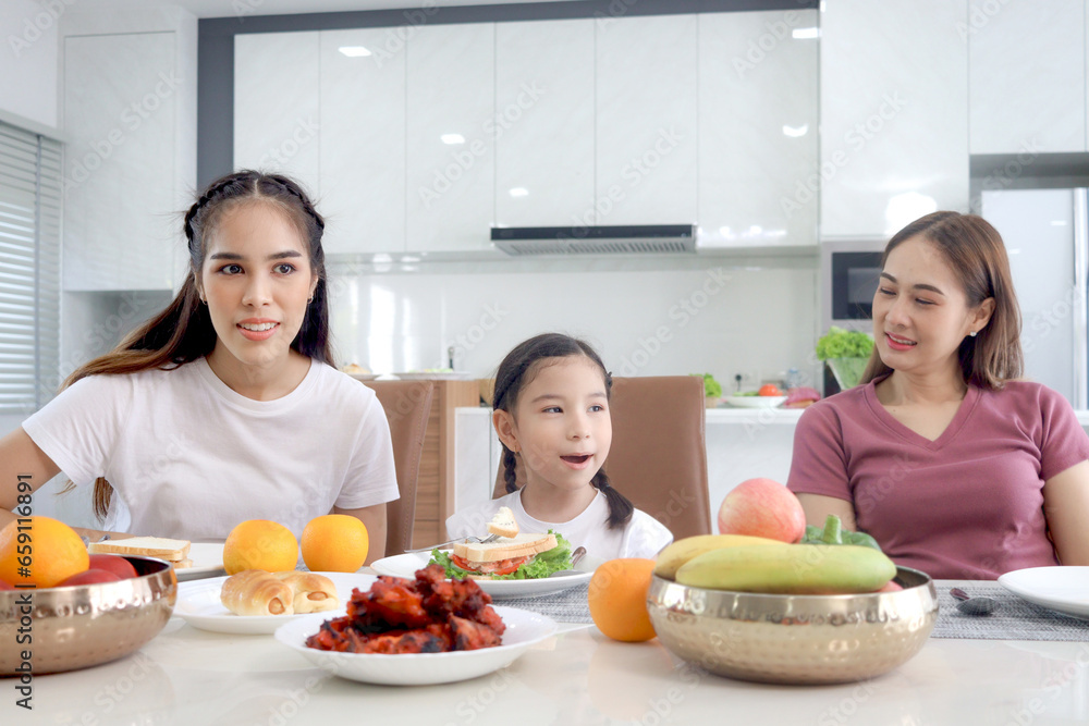 Happy family has meal in dining room. Parent mother, daughter and aunt sitting around dining table and having fun during breakfast. Cheerful family enjoy spending time together.