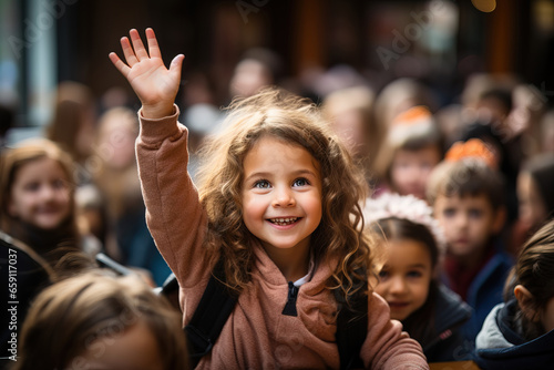 A happy, smiling girl with her hand raised in the air at school among her classmates © Volodymyr