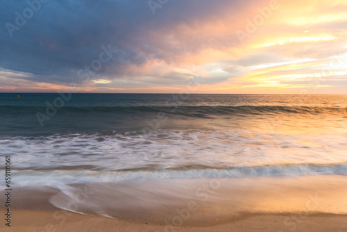 Sunset on sandy beach with ocean waves and colorful sky and clouds, Algarve, Portugal