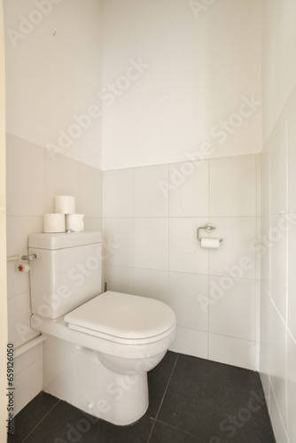 a white toilet in a bathroom with black tiles on the floor and walls behind it is a roll of toilet paper