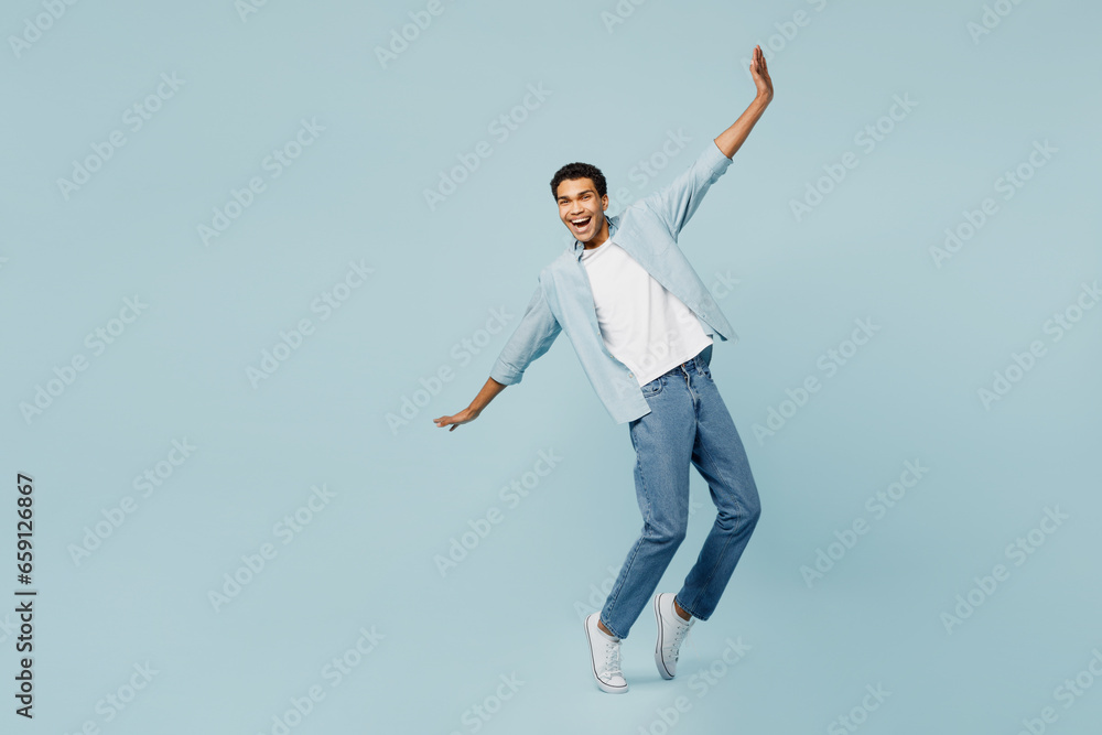 Full body young man of African American ethnicity wear shirt casual clothes stand on toes lean back with outstretched hands dance isolated on plain pastel light blue cyan background studio portrait