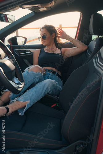 Pretty woman with sunglasses is posing inside of a car at sunset