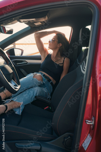 Pretty woman with sunglasses is posing inside of a car at sunset © Cristian Blázquez
