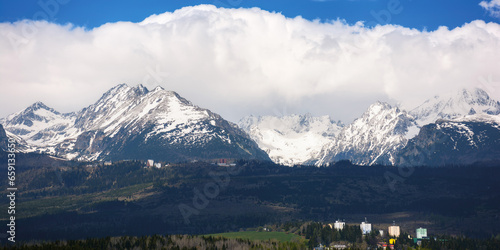 nature background of mighty high tatra ridge in spring at high noon. snow capped rocky peaks beneath a cloudy sky