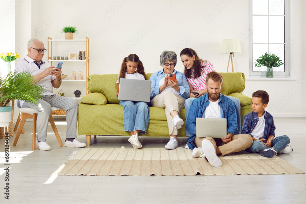 Big family sitting in living room with gadgets, parents, grandparents and two children. Grandpa, mom and grandma looking at smartphones screens, daughter and father working on laptops with son. Big family sitting in living room with gadgets, parents, grandparents and two children. Grandpa, mom and grandma looking at smartphones screens, daughter and father working on laptops with son.