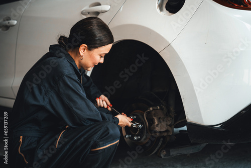 Hardworking female mechanic changing car wheel in auto repair workshop. Automotive service worker changing leaking rubber tire in concept of professional car care and maintenance. Oxus photo