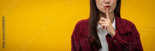 Woman confidence touching finger on lips to making silence gesture isolated over yellow background