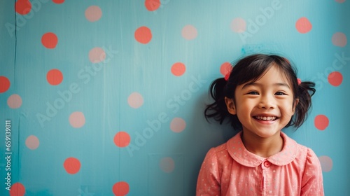 Happy cute Asian toddler girl wearing Polkadot colorful dress smiling and standing in front of blue and red painted wall, girl portrait with copy space. photo