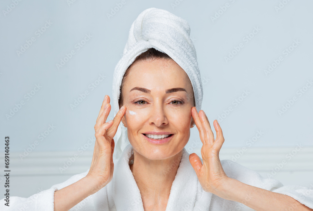 Woman applying cream, towel turban on, smiling Woman applying cream, towel turban on, smiling