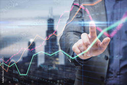 Close up of businessman hand pointing at creative business graph with index and grid on blurry city background. Stock market and financial statistics concept. Double exposure.