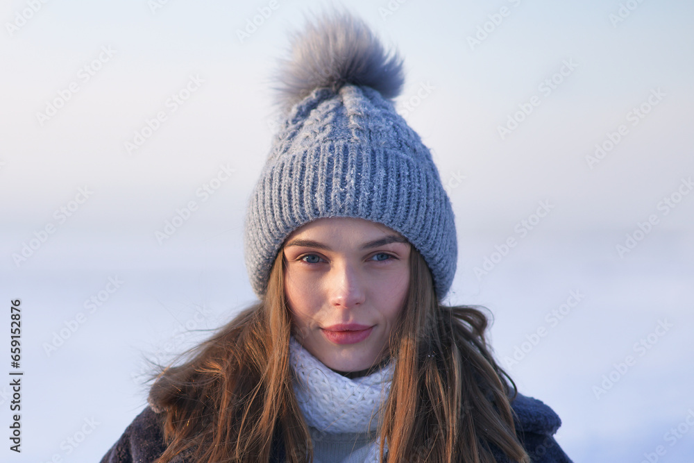 Portrait of beautiful girl young frozen pretty woman standing walking in winter snowy park at cold snow frosty day in hat, scarf, in gloves looking at camera Portrait of beautiful girl young frozen pretty woman standing walking in winter snowy park at cold snow frosty day in hat, scarf, in gloves looking at camera