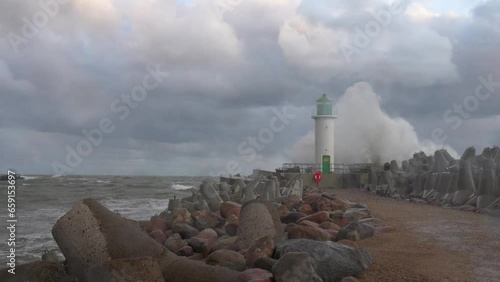 Waves crashing against the lighthouse a moment before the sunset during a storm