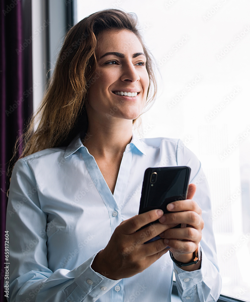 Content female holding phone looking outside window Content female holding phone looking outside window