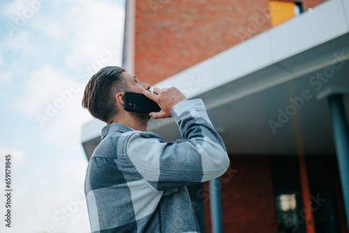 This image portrays a young adult in a candid phone discussion, his back facing us, as he navigates the dynamic city surroundings.