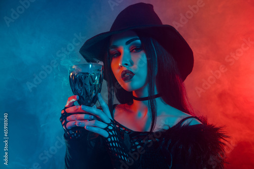 Photo of dark witch warlock hold glass with poisonous liquid magical ritual over neon mist background