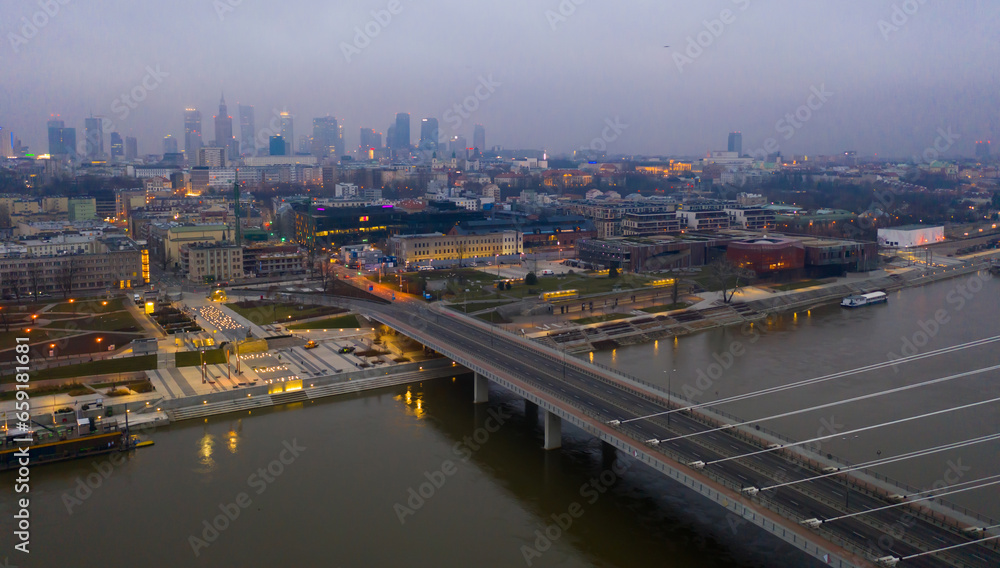 Illuminated cityscape of Warsaw with Vistula river and Swietokrzyski Bridge at dusk, Poland