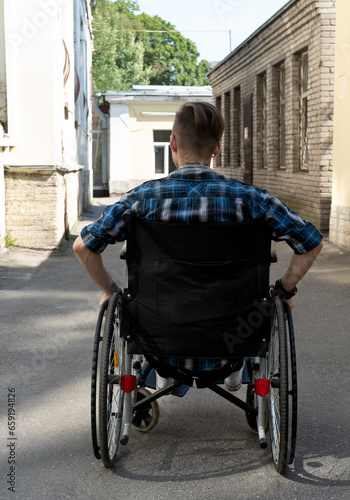 A young disabled man sits in a wheelchair. Walk on a summer day. City background.