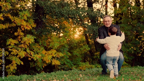 Child, son runs to his Father, hugs her in autumn park, Twirl kid round. Dad plays with her child, spins her joyful son. Happy family, baby. Carefree child happily hugs his Father. Father spins child