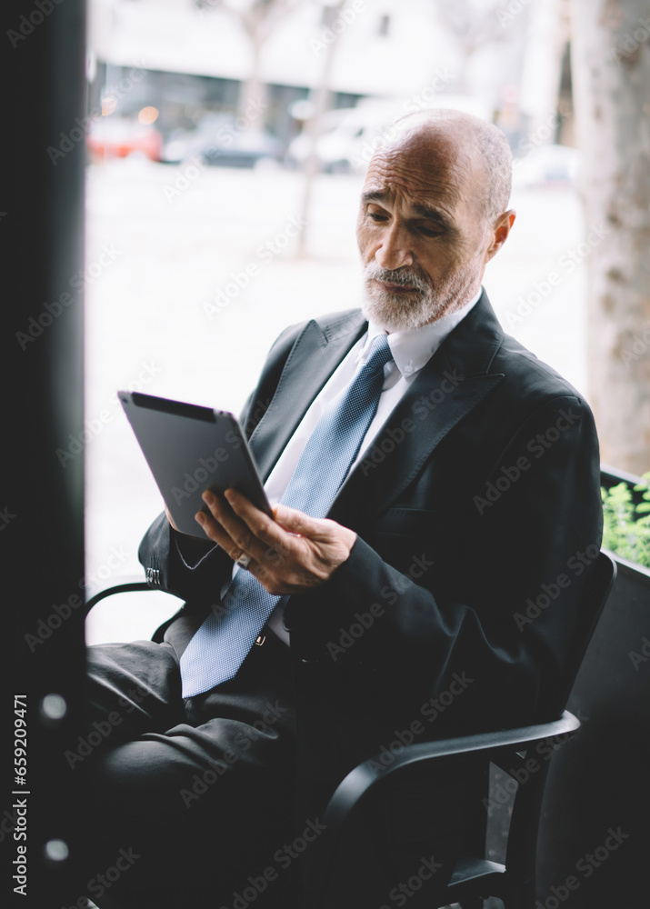 Serious businessman with tablet in cozy street cafe Serious businessman with tablet in cozy street cafe