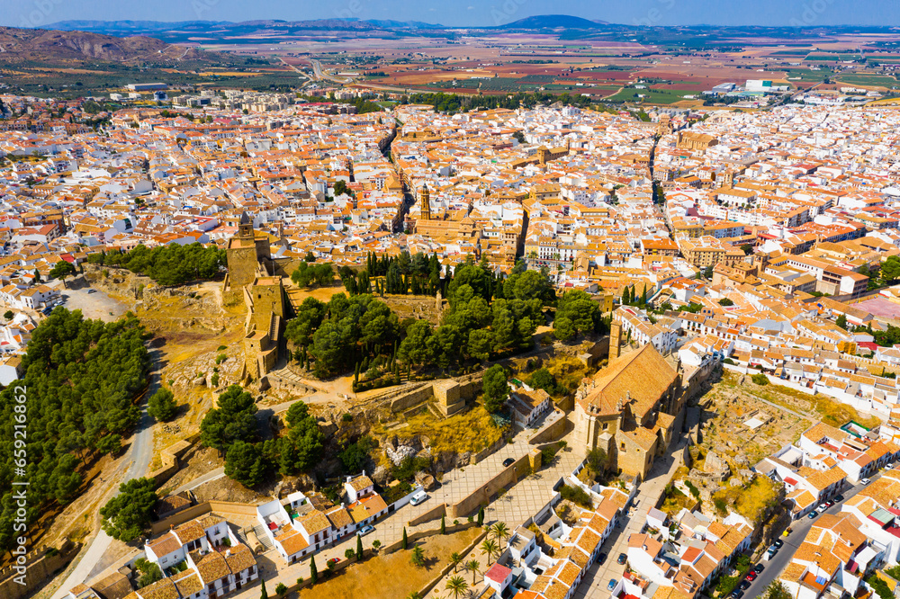 View from drone of Antequera cityscape in sunny fall day overlooking medieval castle and Royal Collegiate Church of Santa Maria la Mayor, Spain..