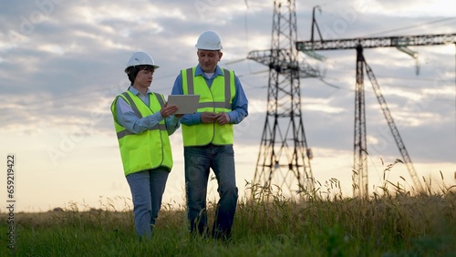 Engineer performs new project on tablet to manager walking past power substation