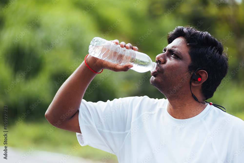 Close up Asian young sport runner black man wear athlete headphones he drinking water from a bottle after running at the outdoor street health park, healthy exercise workout concept Close up Asian young sport runner black man wear athlete headphones he drinking water from a bottle after running at the outdoor street health park, healthy exercise workout concept