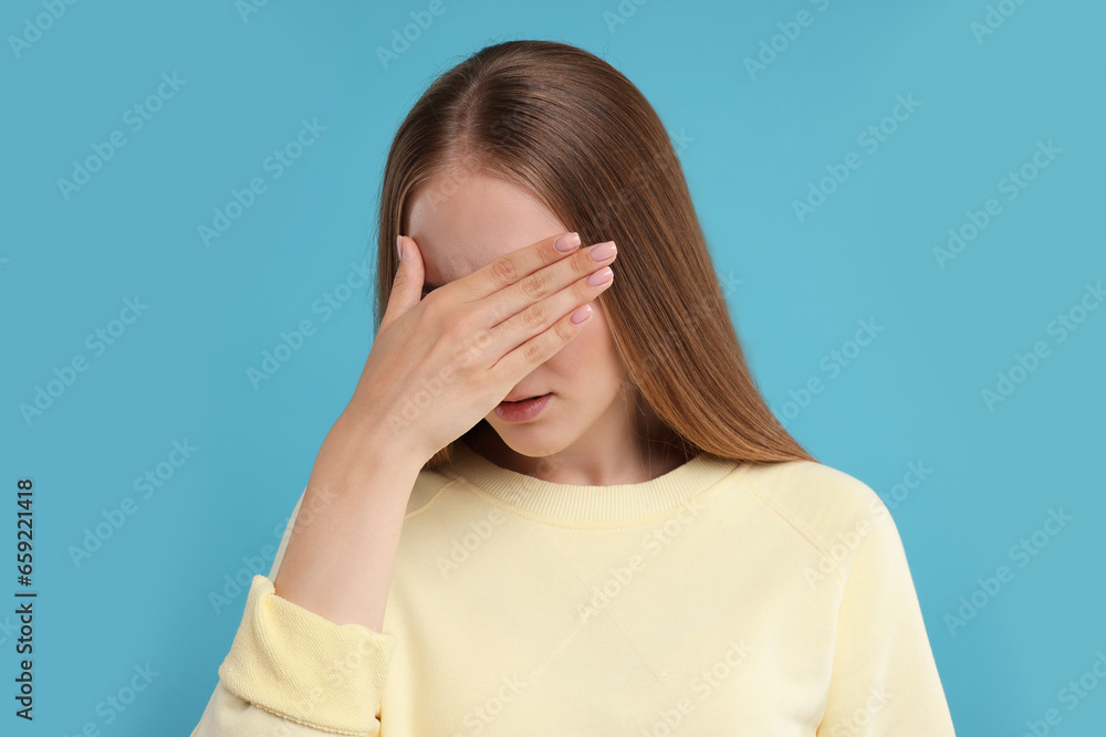 Embarrassed woman covering face with hand on light blue background Embarrassed woman covering face with hand on light blue background