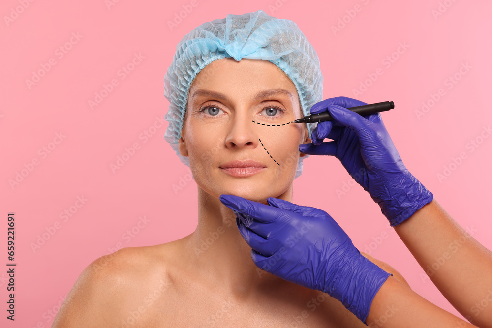 Woman preparing for cosmetic surgery, pink background. Doctor drawing markings on her face, closeup Woman preparing for cosmetic surgery, pink background. Doctor drawing markings on her face, closeup