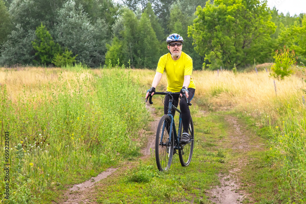 Fototapeta premium bearded man cyclist in yellow clothes rides a bike on a road in nature. sports, hobbies and entertainment for health