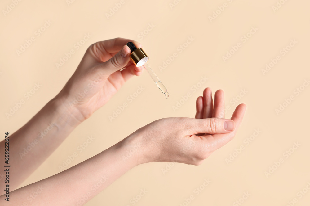 Woman dripping cosmetic oil onto hand against beige background, closeup