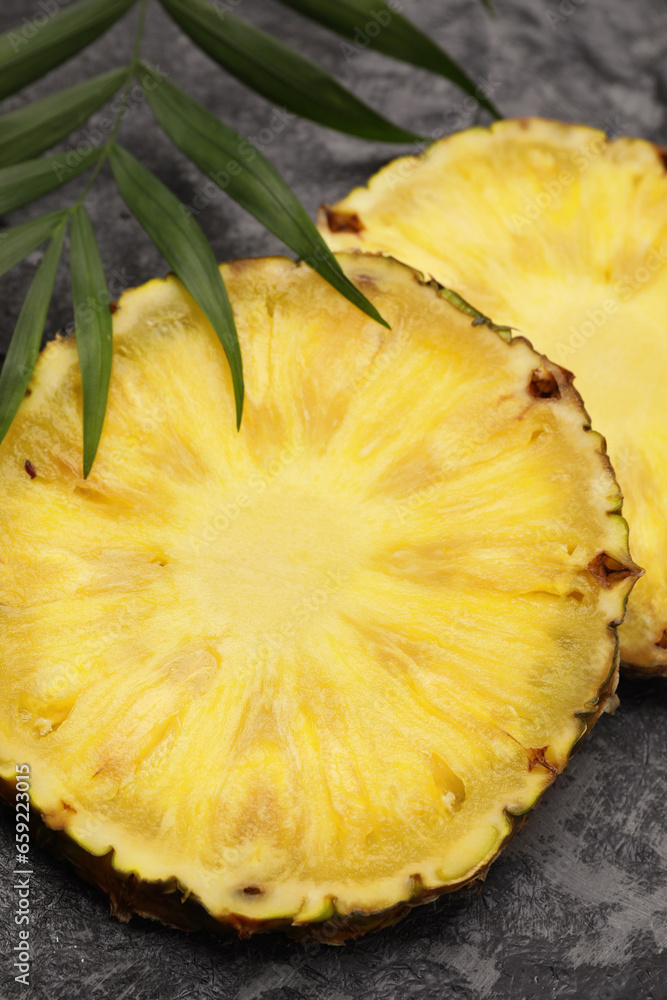 Slices of tasty ripe pineapple and green leaves on black textured table, closeup Slices of tasty ripe pineapple and green leaves on black textured table, closeup