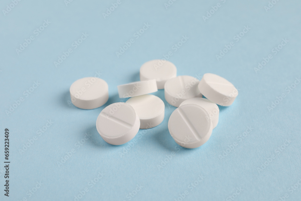 Pile of white pills on light blue background, closeup Pile of white pills on light blue background, closeup