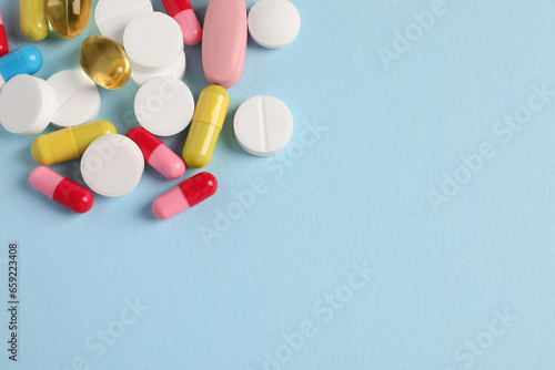 Pile of colorful pills on light blue background, flat lay. Space for text