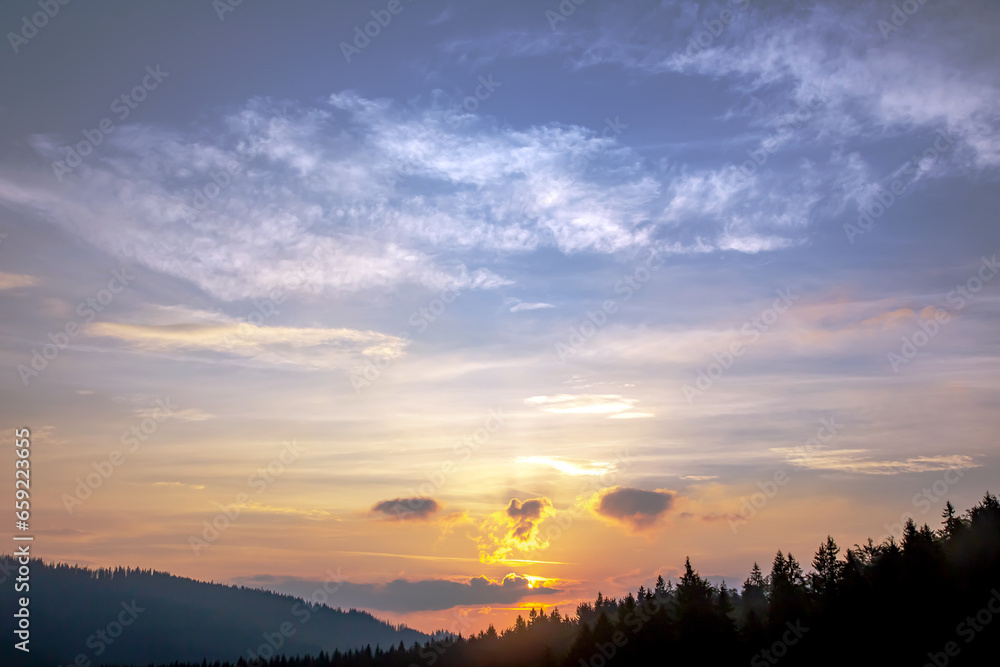 Fototapeta premium Colorful clouds in the sky at sunset against the backdrop of a mountainous forest area.