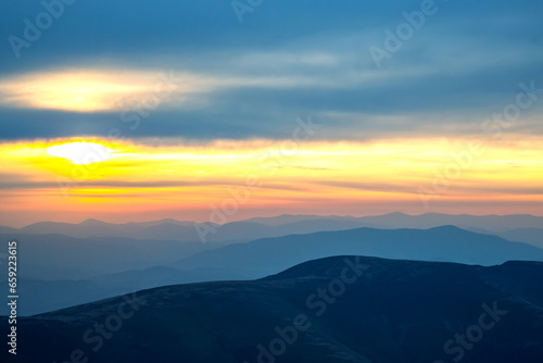 Colorful clouds in the sky at sunset against the backdrop of a mountainous forest area. © photosaint