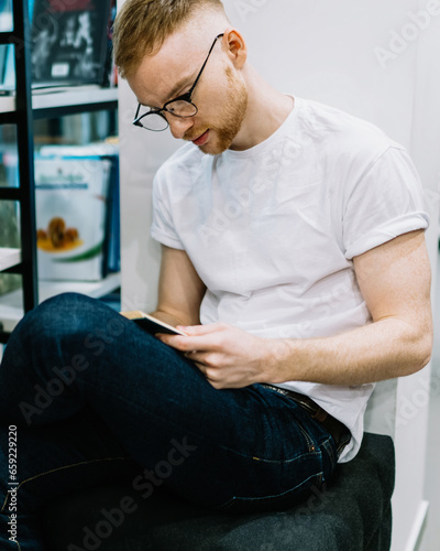Thoughtful guy sitting cross legged and reading book in library