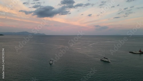 Beautiful Sunset over the Sea. Calm smooth waters of Mediterranean Sea, aerial drone video. Natural landscape with sail boats. Light pink sky, gulf.

