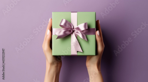 A woman's hands hold a green gift box with a pink bow and ribbons