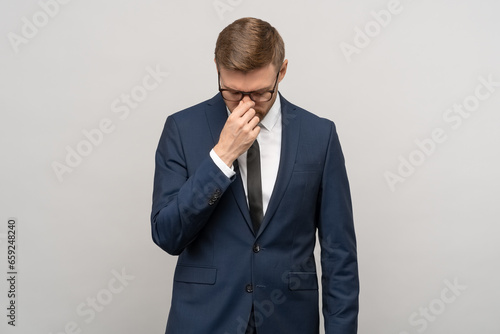 Heartbroken exhausted man, businessman in suit, office worker worried about bankruptcy job loss on grey background. Upset guy feeling bad, headache migraine after busy day, burnout, overwork concept. © DimaBerlin