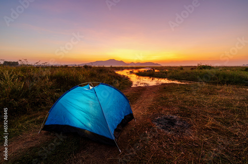 Tourist tent on camping site on the meadow next to the lake during sunset, Thailand. Beautiful sunset twilight sky