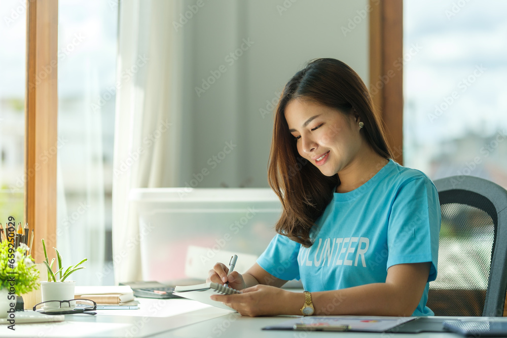 Nice, friendly asian female volunteer wearing volunteer t-shirt working at charity center Nice, friendly asian female volunteer wearing volunteer t-shirt working at charity center