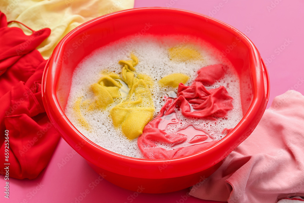 Plastic basin with dirty laundry, water and foam on pink background Plastic basin with dirty laundry, water and foam on pink background