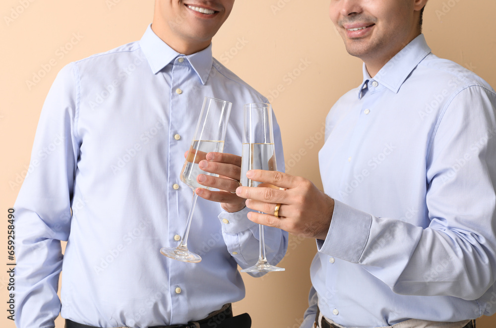 Married gay couple with glasses of champagne on beige background, closeup