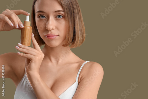 Young woman with bottle of natural serum on green background