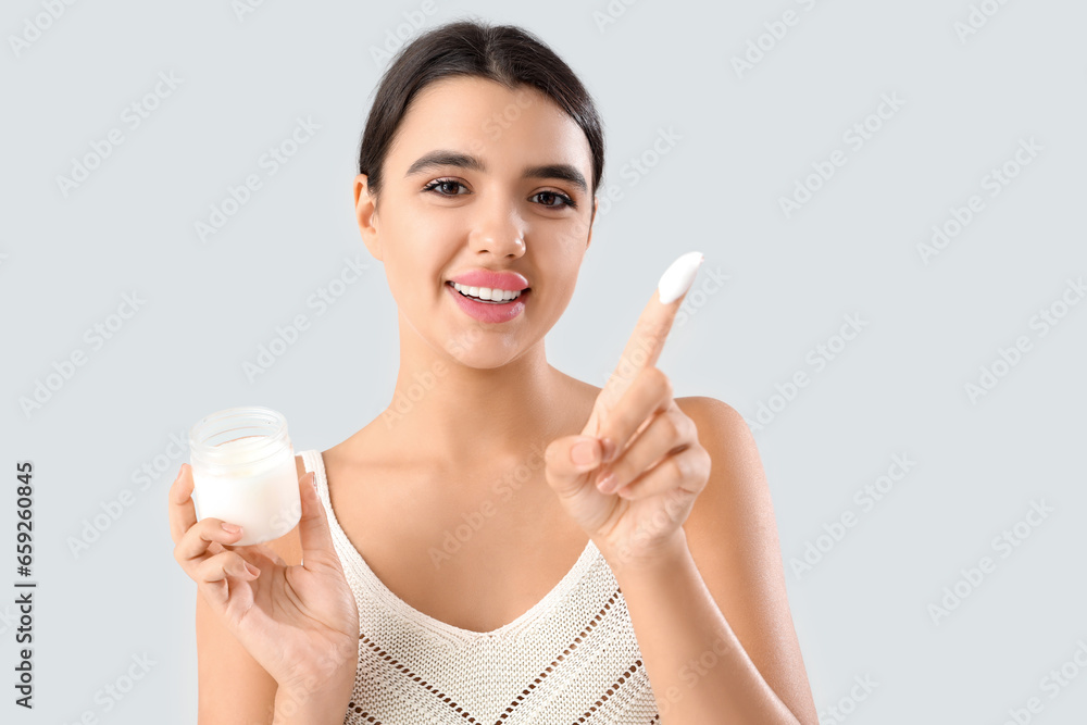Beautiful young woman applying coconut oil on her body against grey background Beautiful young woman applying coconut oil on her body against grey background