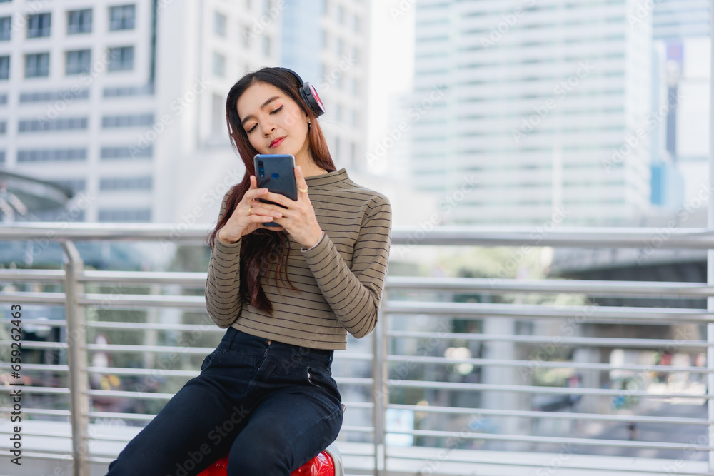 Fototapeta premium Beautiful Asian woman traveler relaxes while listening to music Young Asian tourist waits for public transportation in the city Solo travel itinerary Young female office worker resting on long holiday