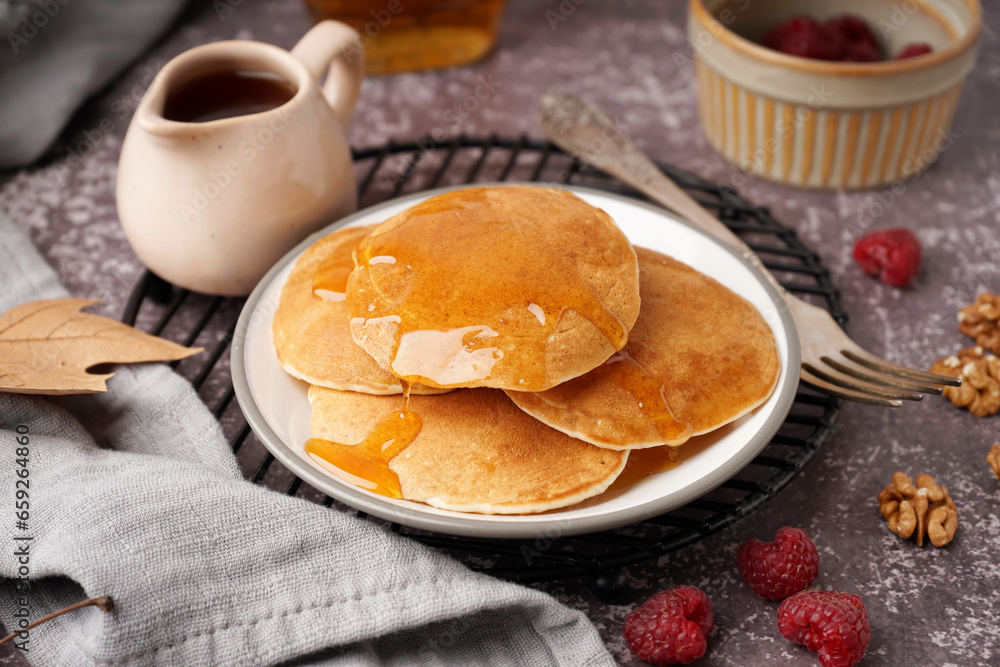 Plate of tasty pancakes with raspberries and maple syrup on grey background